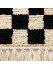 Gros plan sur la texture fibreuse et le relief de la laine d’un tapis damier noir et ivoire