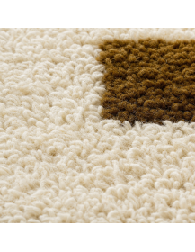 Gros plan sur la texture moelleuse et irrégulière de la laine ivoire et les motifs bruns compacts