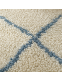Gros plan sur la texture fibreuse et duveteuse de la laine du tapis ivoire écru et bleu gris pâle