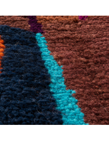 Gros plan sur la laine dense et mate du tapis, ses mèches irrégulières, ses stries horizontales et ses motifs géométriques color