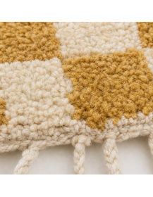 Détail de la texture laineuse bouclée et du relief en damier du tapis ivoire et ocre